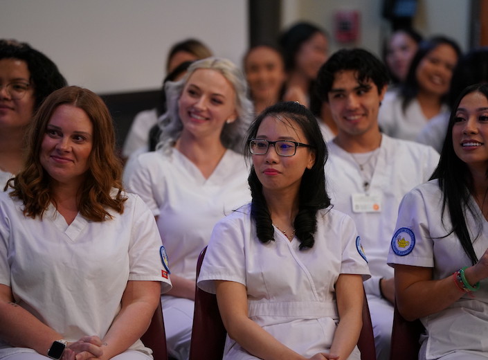 Nursing assistants sit in audience of commencement ceremony in their white scrubs.