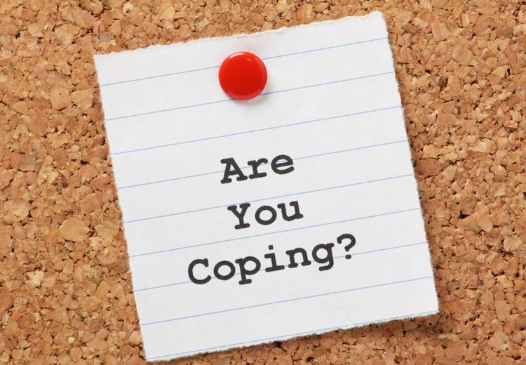"Are you coping?" is written on a piece of white paper and thumbtacked onto a corkboard.