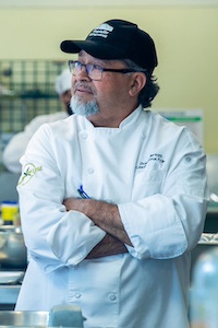 Daniel Arias in chef's whites, black hat, arms crossed in his kitchen.