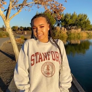 Skarlette, a teenager with long braids and light brown skin, wears an oversized Stanford sweatshirt.