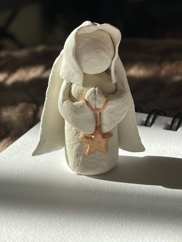 A sculpture of a white clay angel holding a gold star.