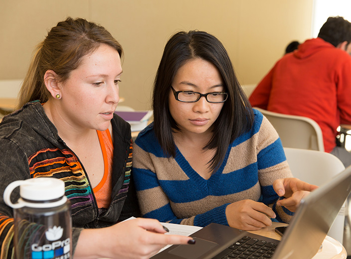 Two female students, one white and the other Asian, work together at a laptop.