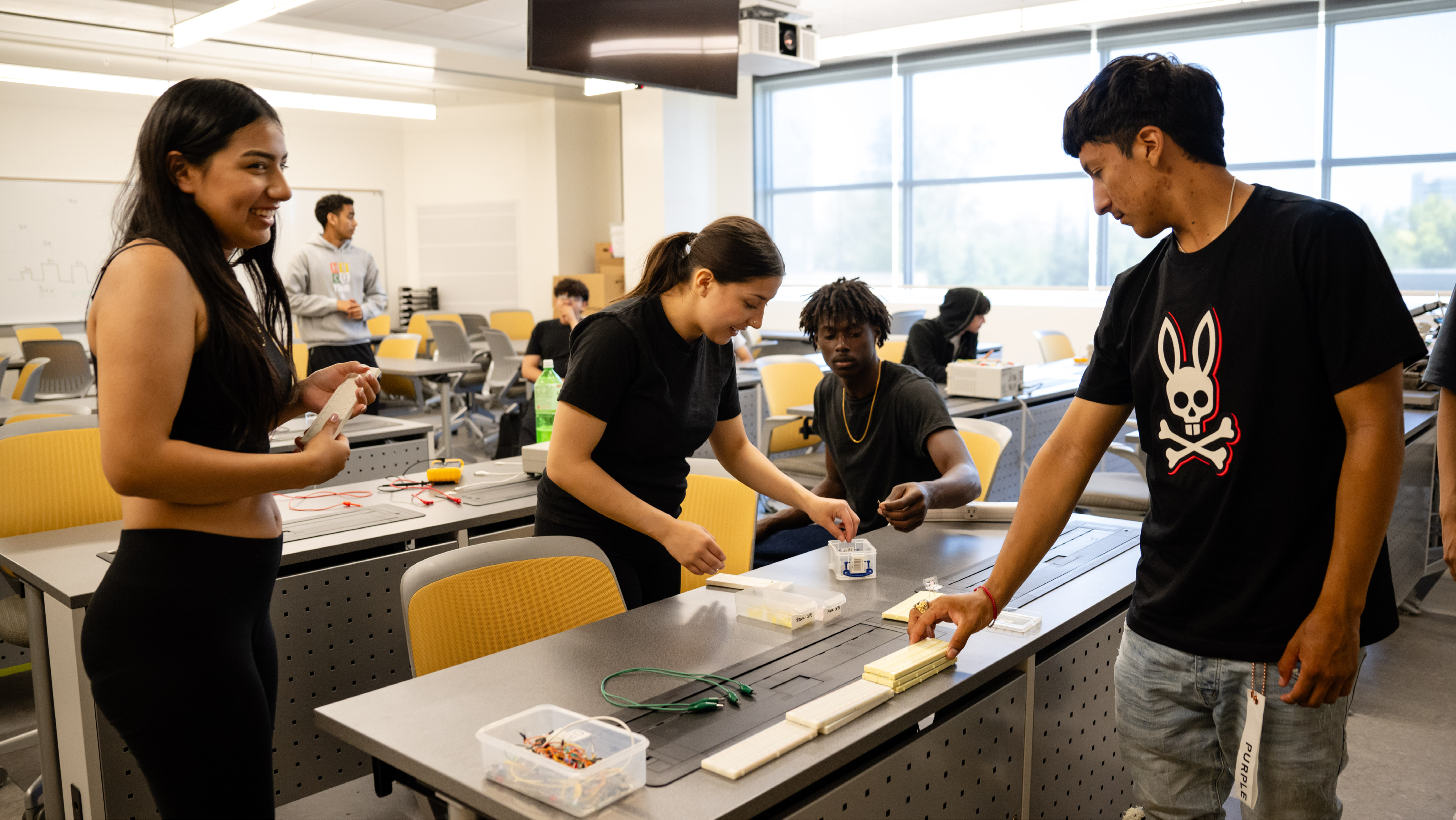 A group of students collaborating and working on hands-on circuit board components around a classroom table.