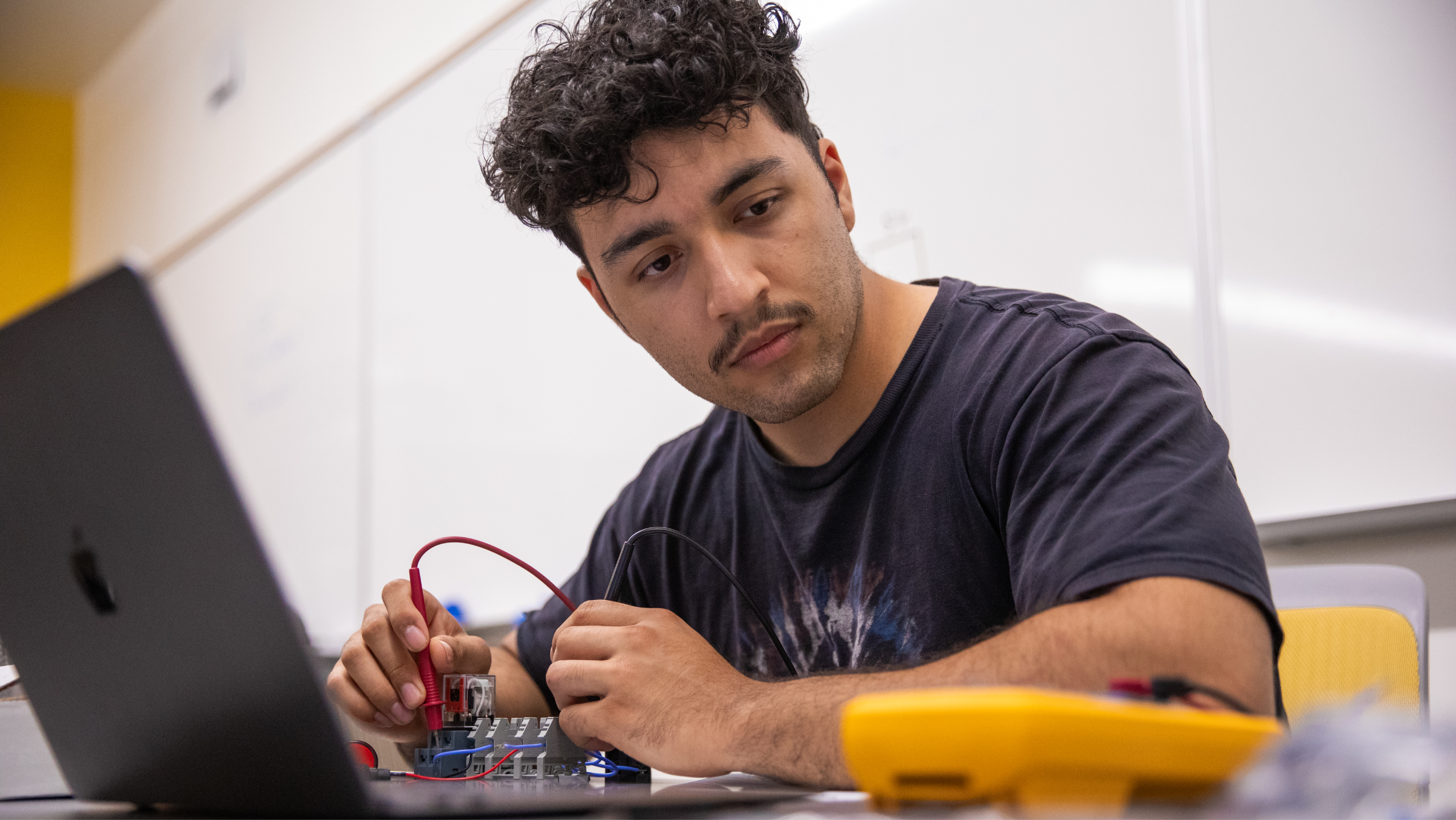 A men in a lab setting closely examining a circuit board and electronic component.