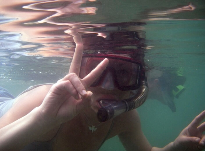 Snorkeling student gives a peace sign underwater to camera.