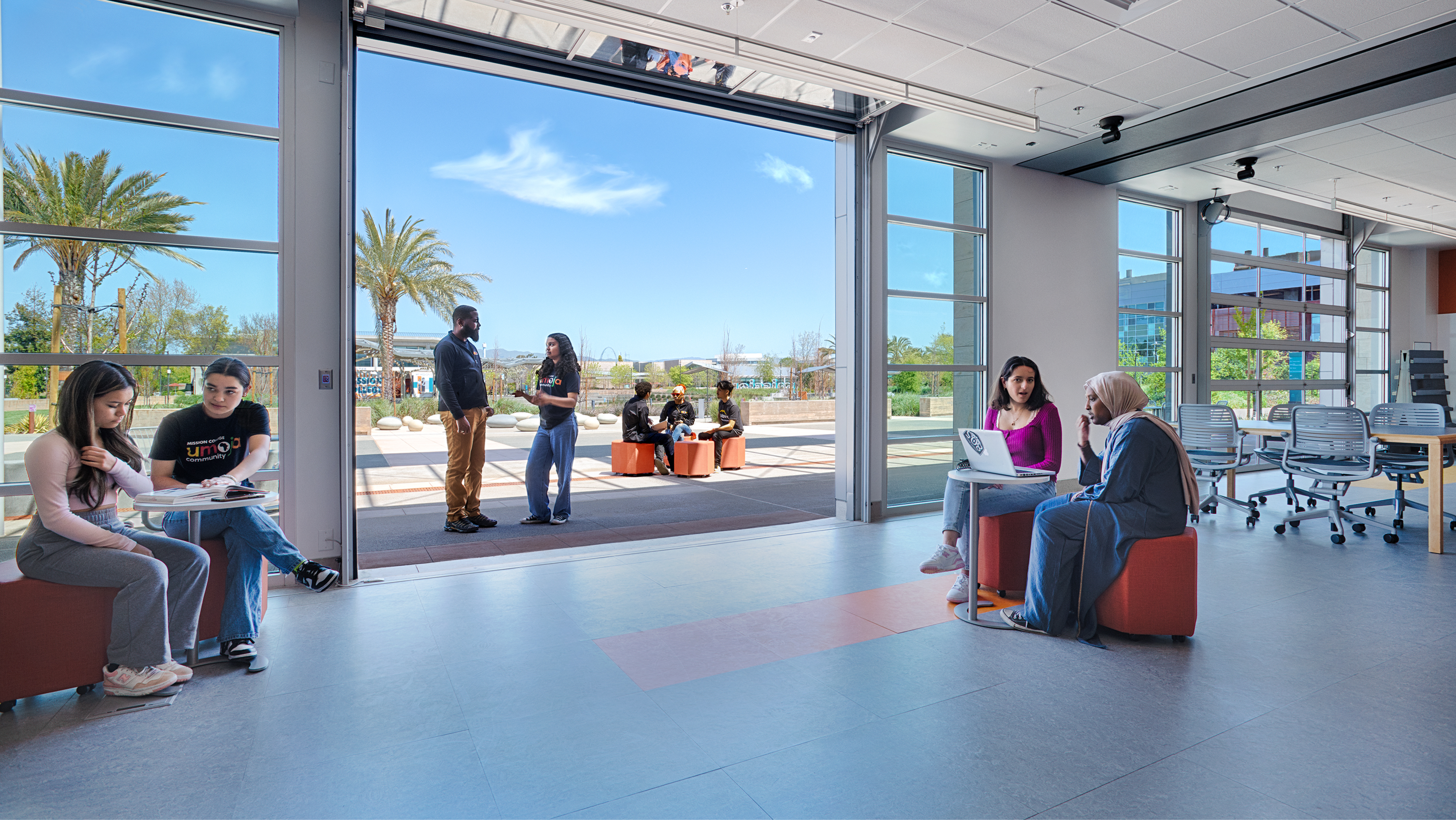 Students sitting and collaborating in a modern study lounge with large glass rollup doors open to the campus.