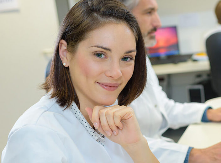 Young woman with chin-length brown hair poses in a classroom computer lab.