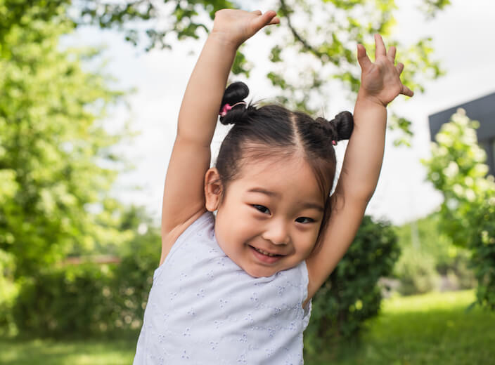 Asian toddler squealing and putting her hands in the air.