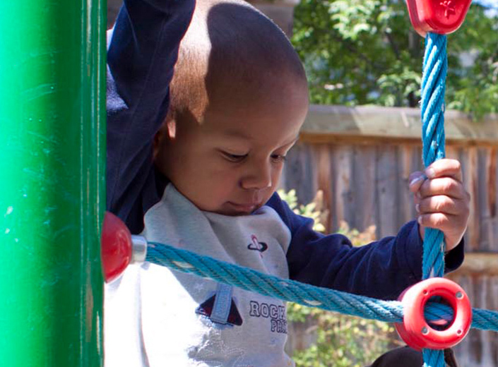 African-American pre-schooler plays on a colorful jungle gym. 