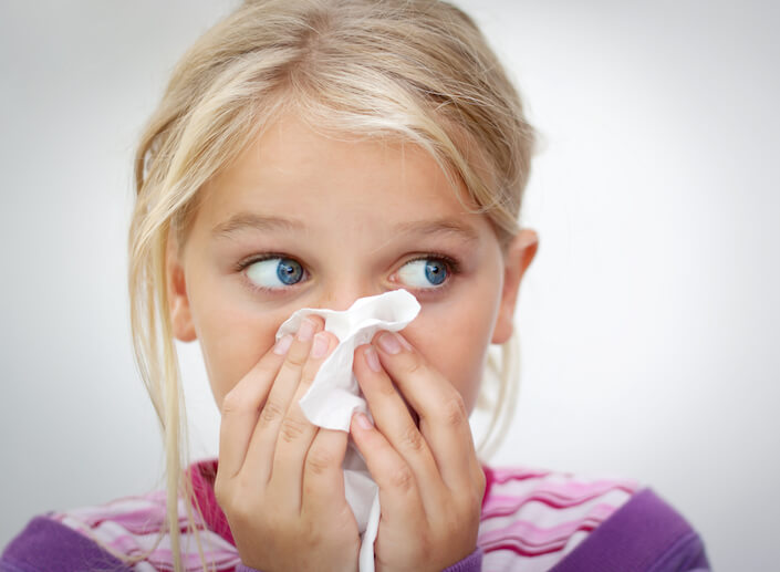A white blonde female child holds a tissue up to her nose.