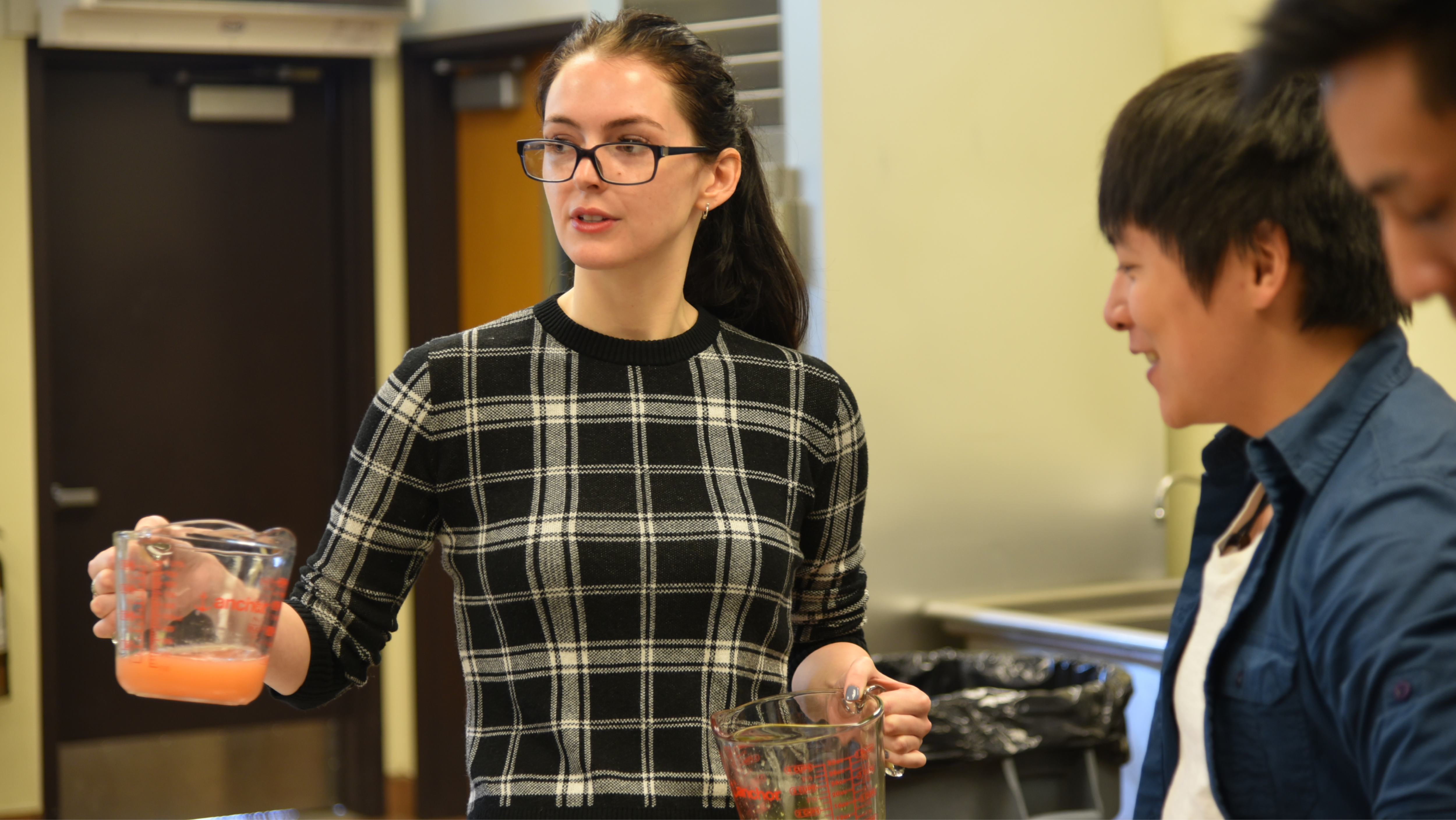 A student wearing glasses holding glass measuring cups during a chemistry lab demonstration.