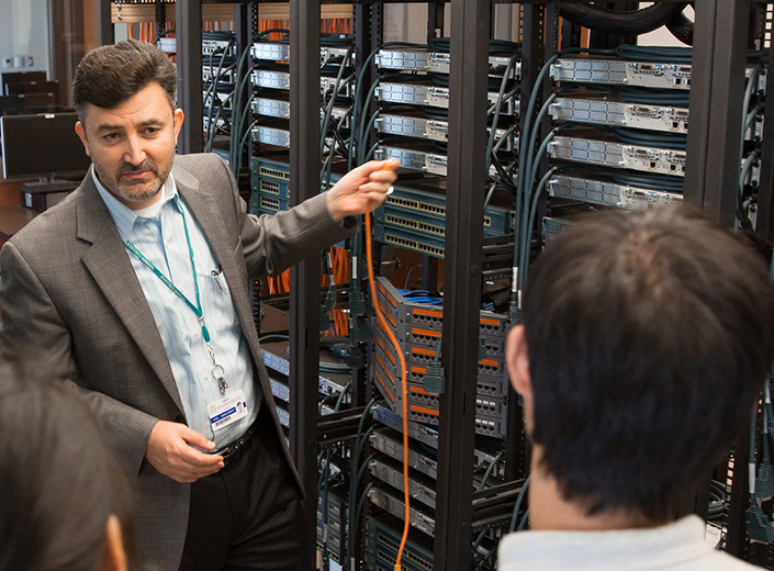 Networking class pays attention to Dr. Wael as he demonstrates a concept in a server room.