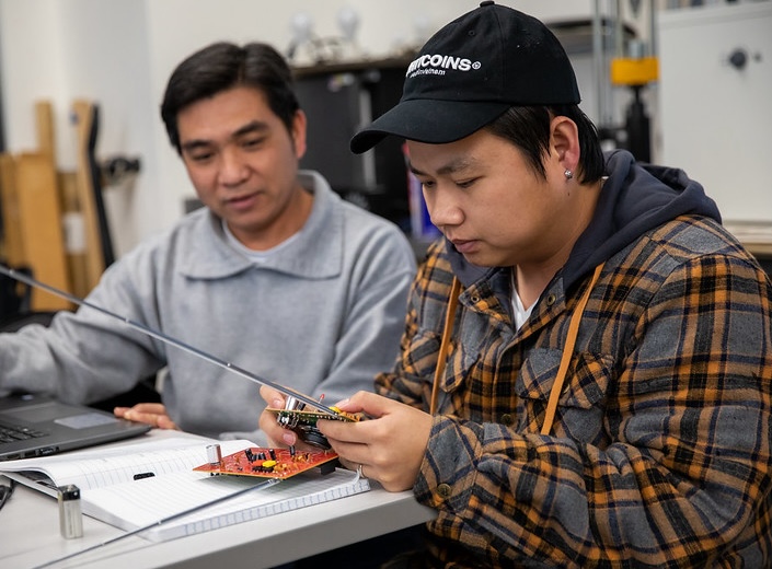 Two male Latino Mechatronics students work with circuit boards.