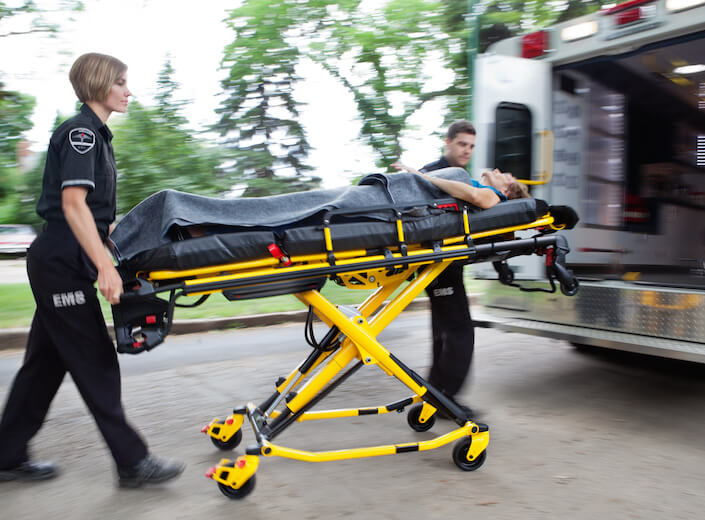 EMTs wheel a stretcher with a person on it toward an ambulance.