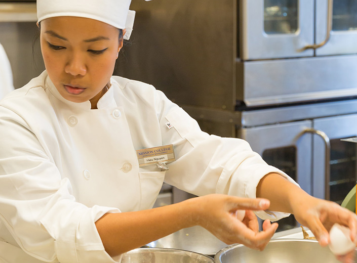 Instructor chef works with two female students in the kitchen