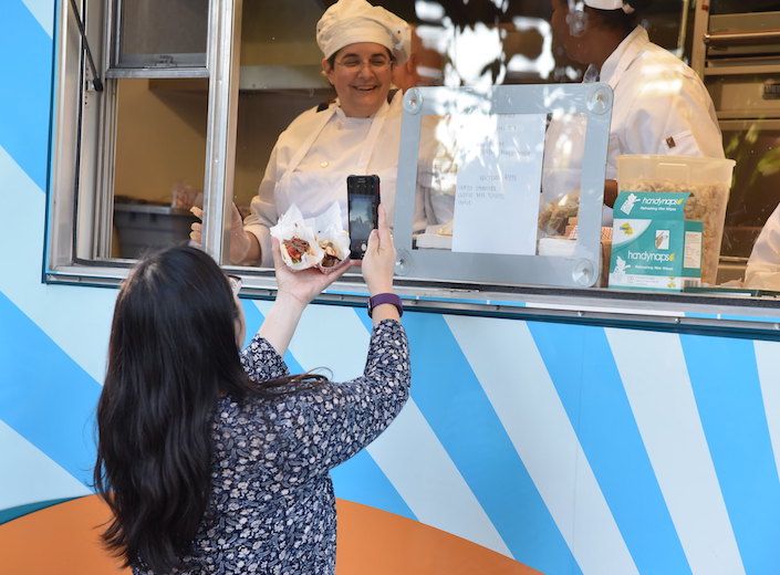 Female Hospitality Management student works in a food truck. She wears a chef's uniform and glasses. 