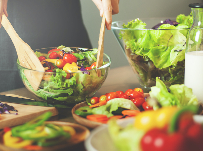 Salad tongs toss a green salad with tomatos, cucumbes, and other veggies.