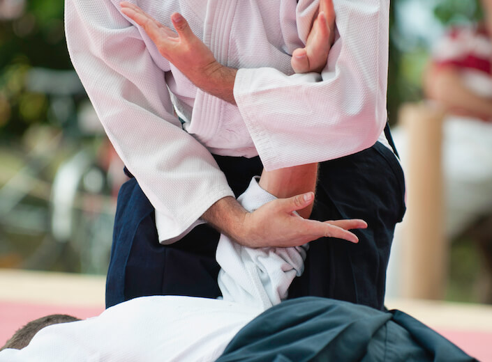 A close-up of two men practicing Aikido. One is pinned and the other crouches above him. Only their torsos and hands are visible.
