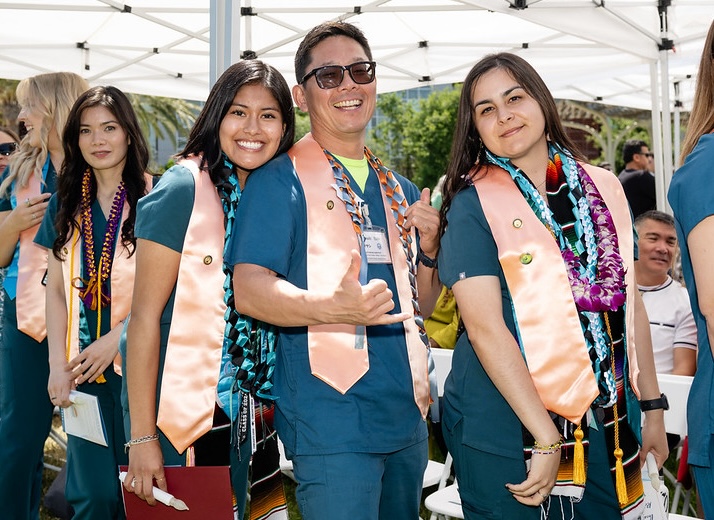 RN graduates, two women and one man, wear teal scrubs and pose for a photo on commencement.