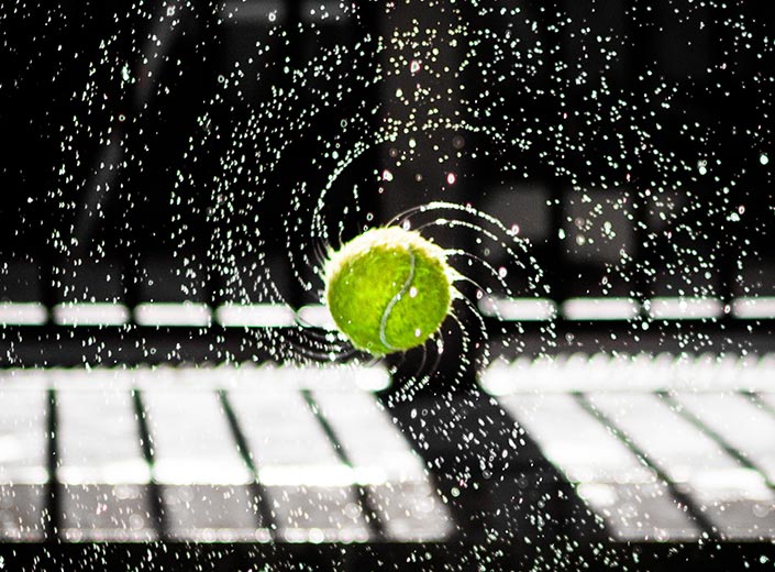 A tennis ball is suspended in mid spin. Water drops are flying off it on all sides.