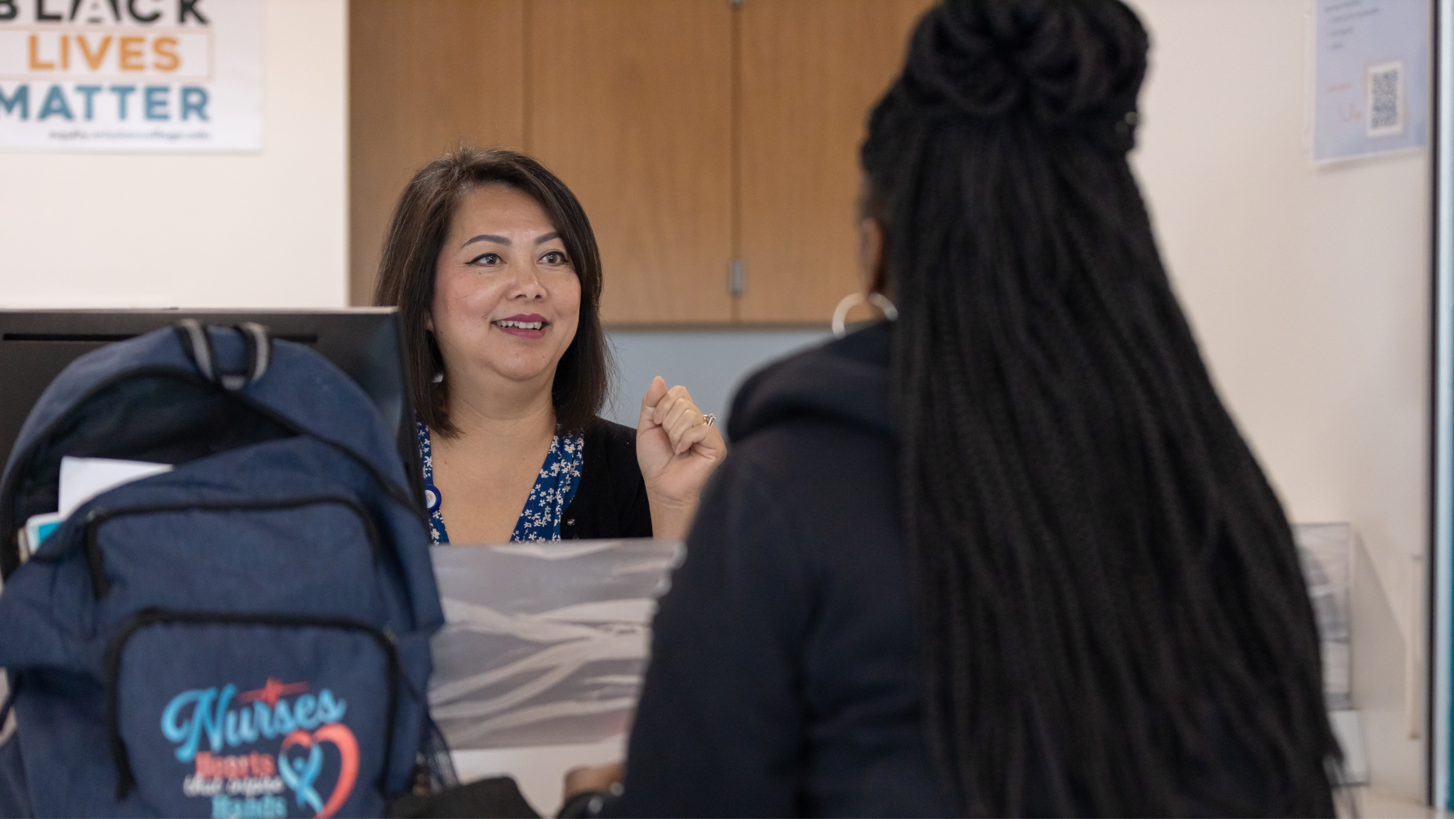 A smiling campus staff member assisting a student at a service desk.