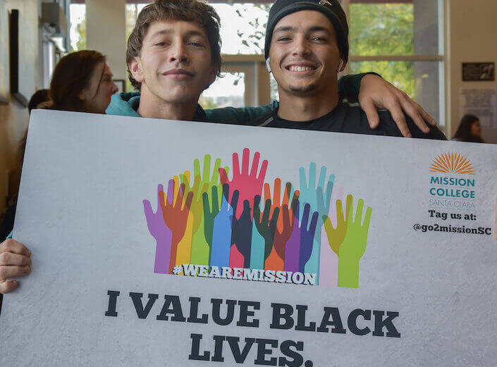 A white male student and a Latinx male student hold a sign that reads "I value Black lives" with colorful handprints decorating it.