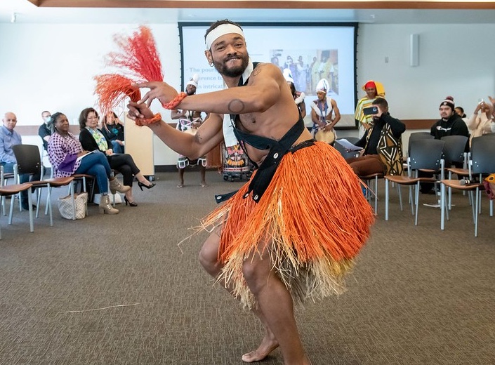 Man in grass skirt and palm fronds performs at Kwanzaa celebration.