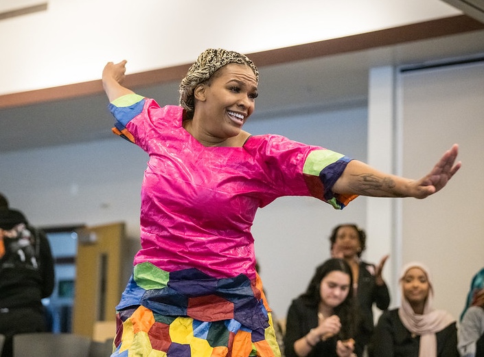 Woman in bright pink shirt and traditional clothing performs at Kwanzaa celebration.