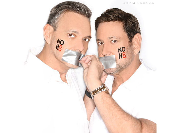 NoH8 portrait of two men, one with dark hair and the other with blonde/light hair with masking tape over their mouths.