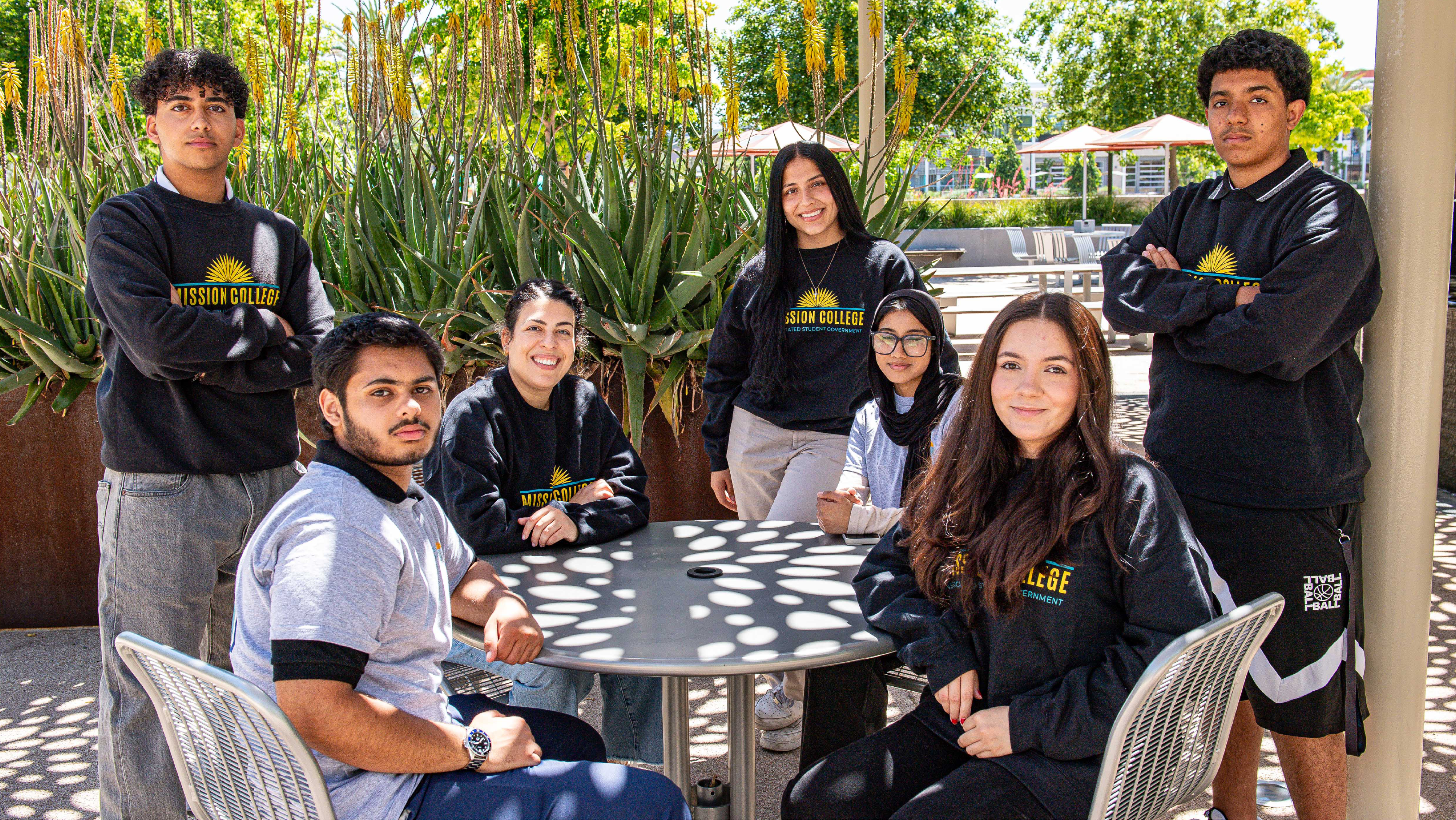 A group of seven ASG student leaders gathered around an outdoor patio table, smiling toward the camera.