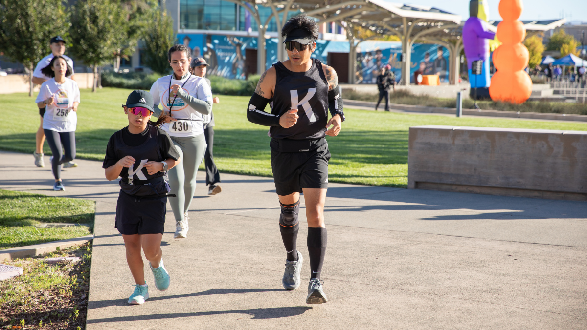 Participants run along the scenic Mission College campus during the Monster Dash & Bash 5K with Halloween decorations in the background.