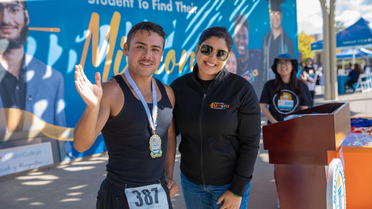 A race participant wearing a finisher medal smiles with a Mission College staff member after completing the Monster Dash & Bash 5K.