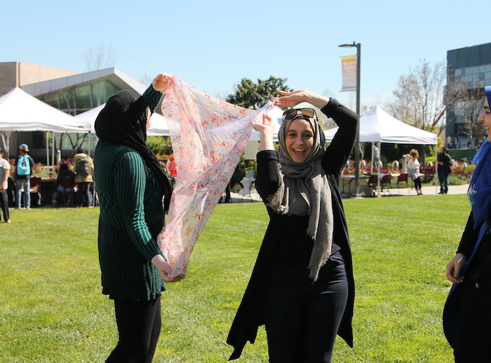 Two women in head scarves dance playfully on the Central Plaza during a college event.
