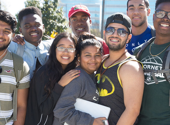 A group of multi-ethnic college students pose together outside on a college campus.
