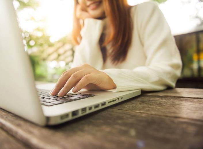 Young woman in white top works on a laptop.