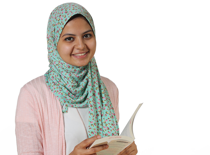 Young woman in hijab holds a book and smiles.