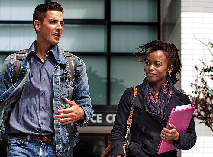 African-American female student with long braids and male Latinx student walk outside talking.