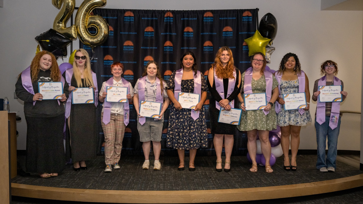 A group photo of adults posing indoors with purple stoles and framed award certificates against a Mission College backdrop, framed by purple and gold balloon towers.