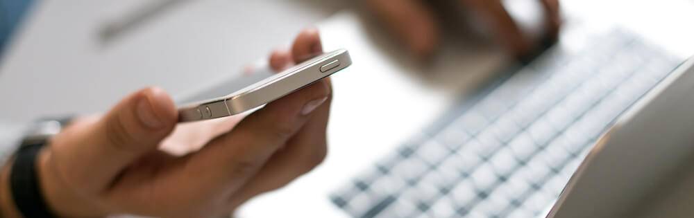 Hands are pictured working on a laptop and holding a smart phone.