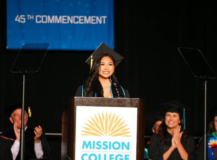 Young woman at commencement in cap and gown. She is of Asian-American descent and has long shiny black hair.