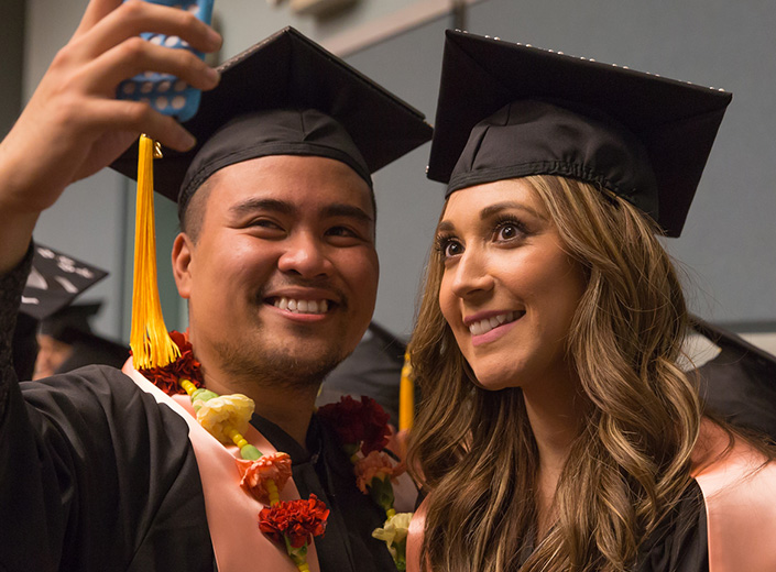 A young man and woman pose for a selfie at Commencement.