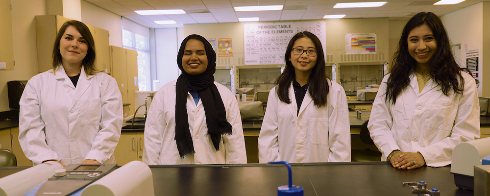 Four female students stand next to each other in a Chemistry lab.