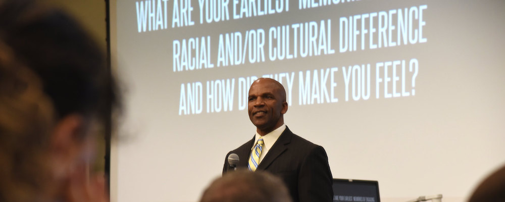 Equity event with a speaker. He stands in front of a projected presentation in a classroom.