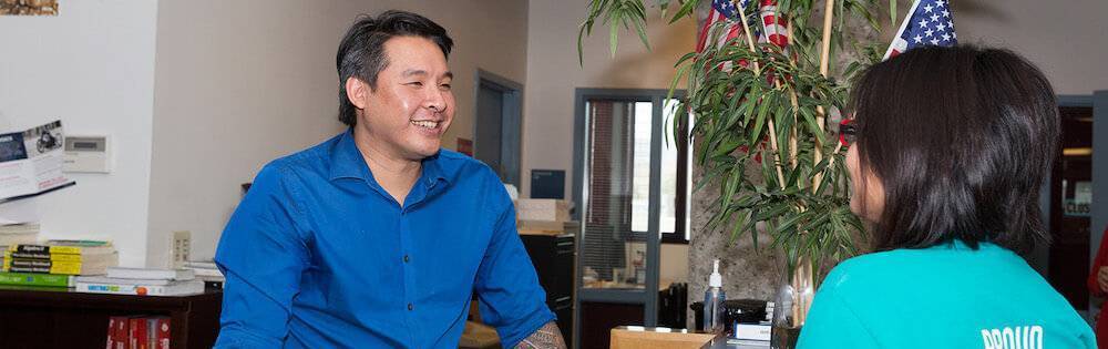 Helpful Asian-American male staff member assists a student in a college student services office.