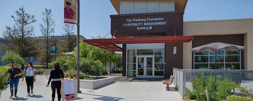 The front of the Hospitality Management building on the Mission College campus is shown. Students walk by.