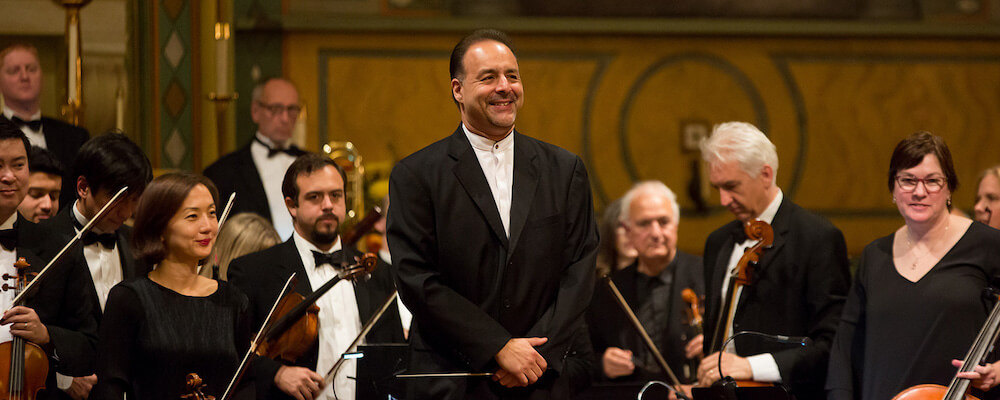 Orchestra performance. Conductor Joseph Ordaz stands facing audience and musicians behind him.