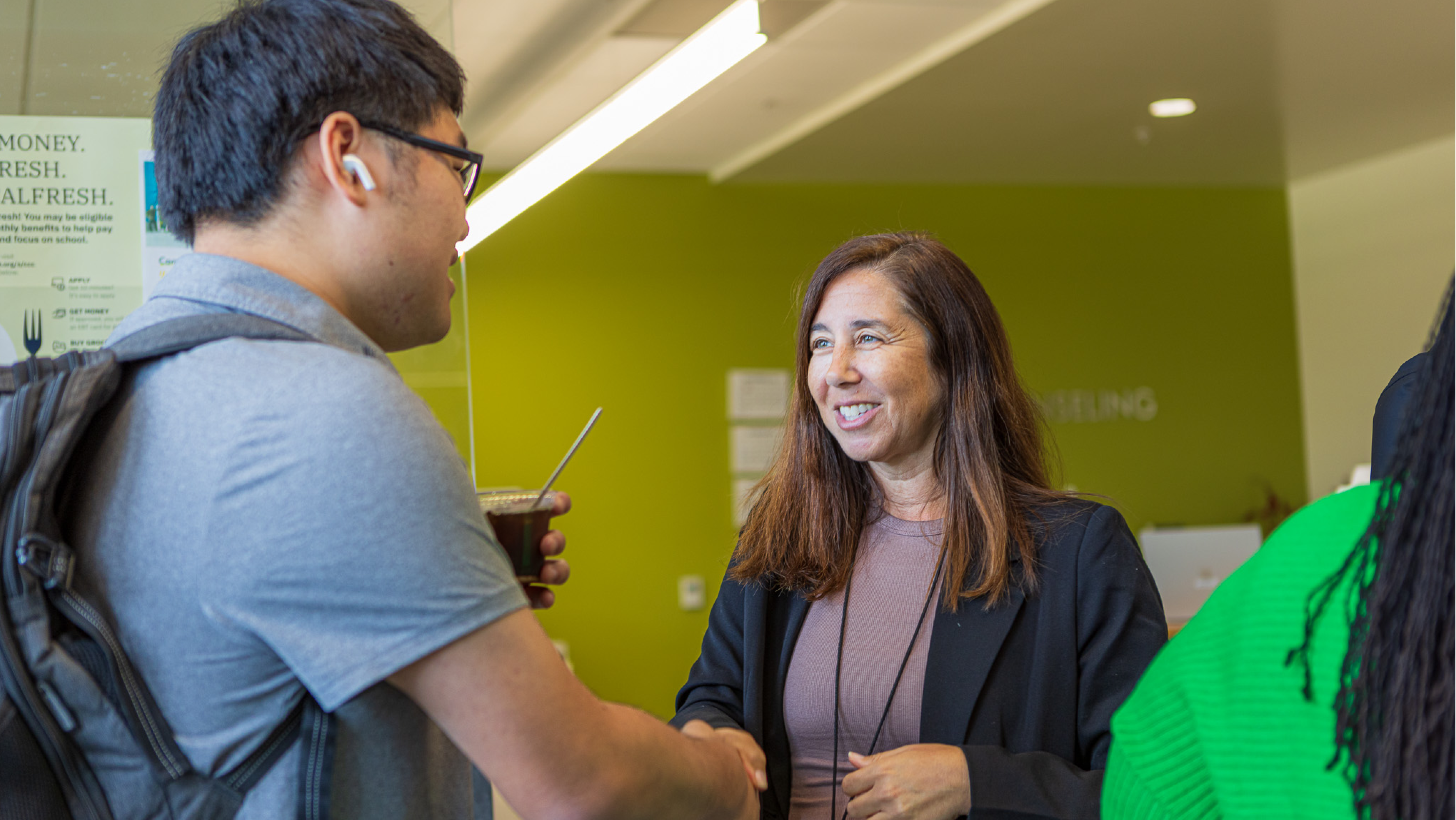 A smiling female counselor greeting and shaking hands with a student wearing a backpack in the counseling center.