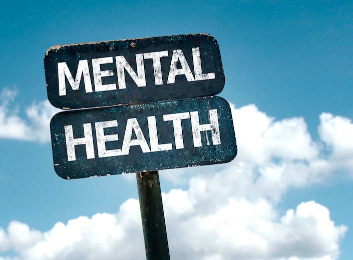 Mental Health is displayed on a road sign against a blue sky with light fluffy clouds.