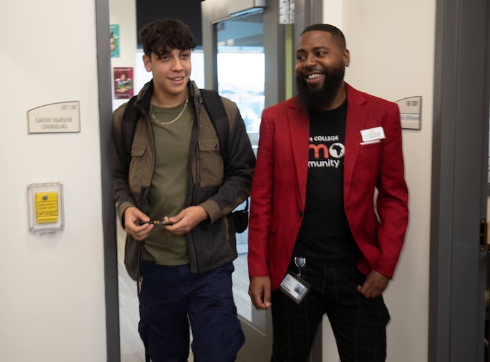Roshawn Walters wears a red blazer and walks with a student in the Counseling Office.