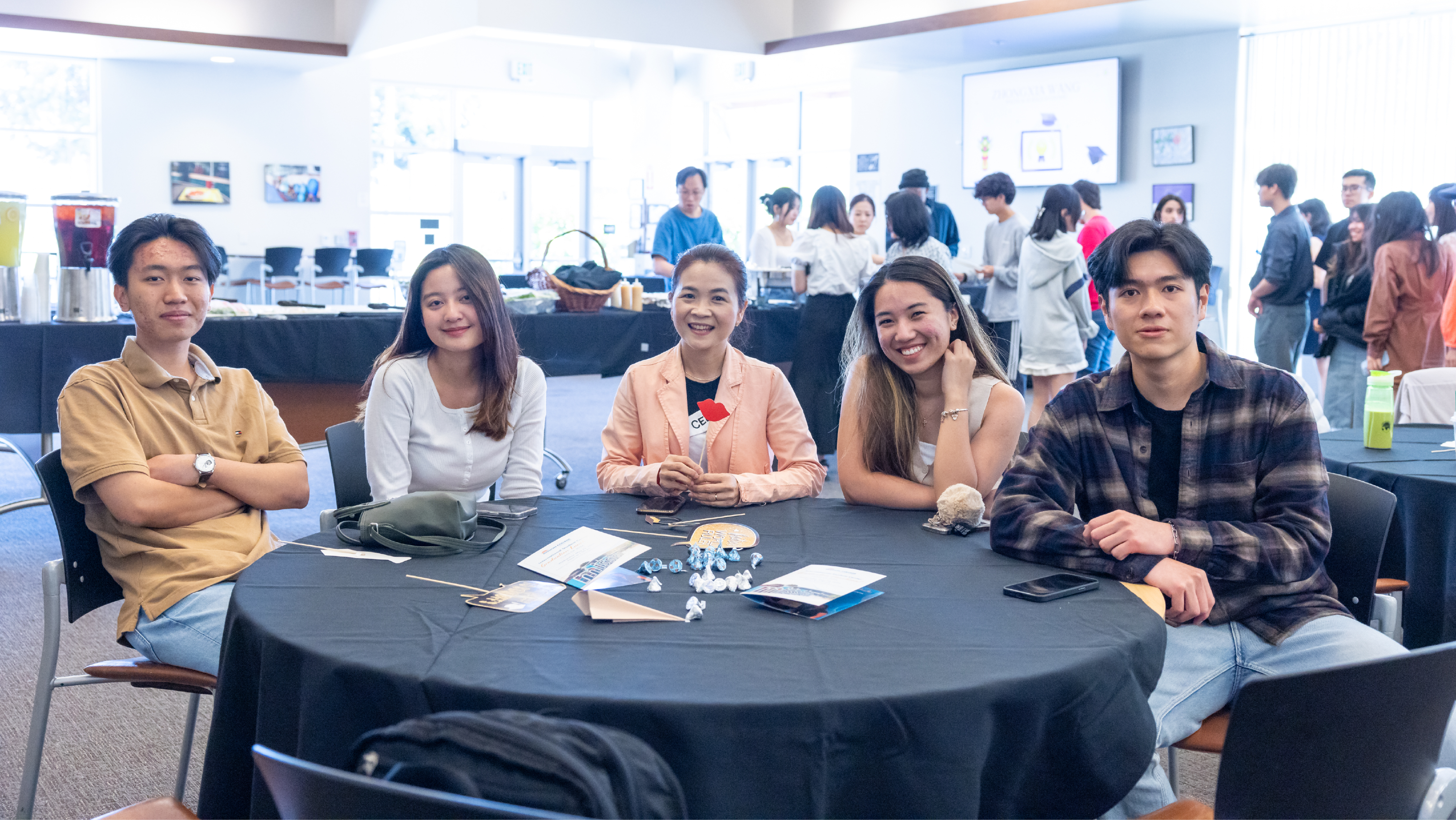 A group of five international students sitting together at a round banquet table during a campus event.